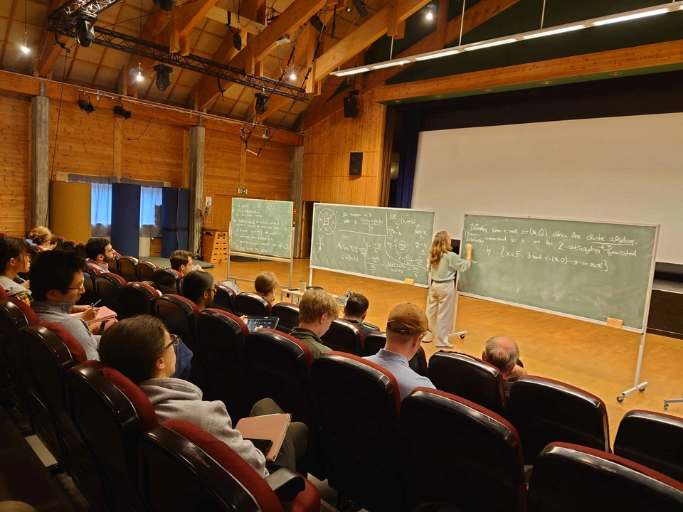 Lara Bossinger lectures at a blackboard while summer-school participants listen.