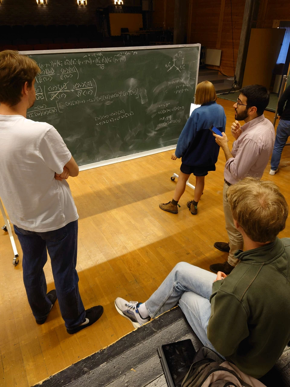 Summer-school participants discuss an exercise around a blackboard.